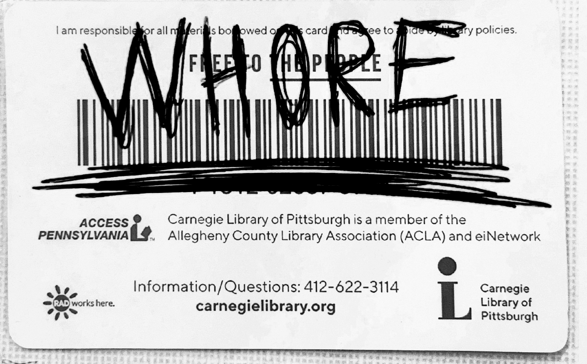 A library card which has "WHORE" written on it in scratchy lettering.